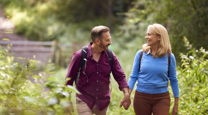 Mature Loving Couple In Countryside Hiking Along Path Through Forest Together Holding Hands